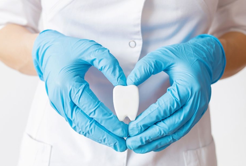 Mani con guanti che formano un cuore con al centro un dente