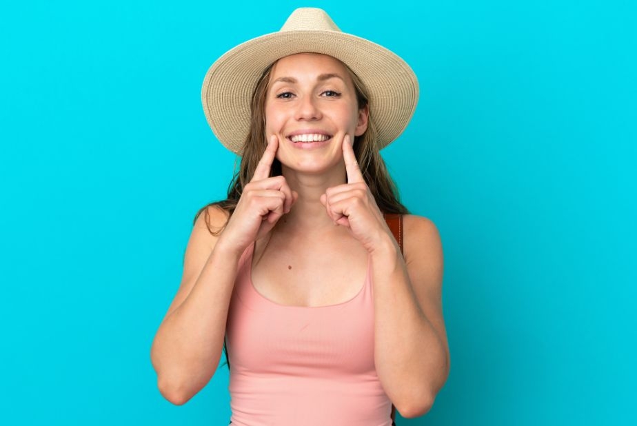 Come prevenire lo squilibrio batterico e proteggere la salute orale in estate ragazza con cappello di paglia che indica sorriso