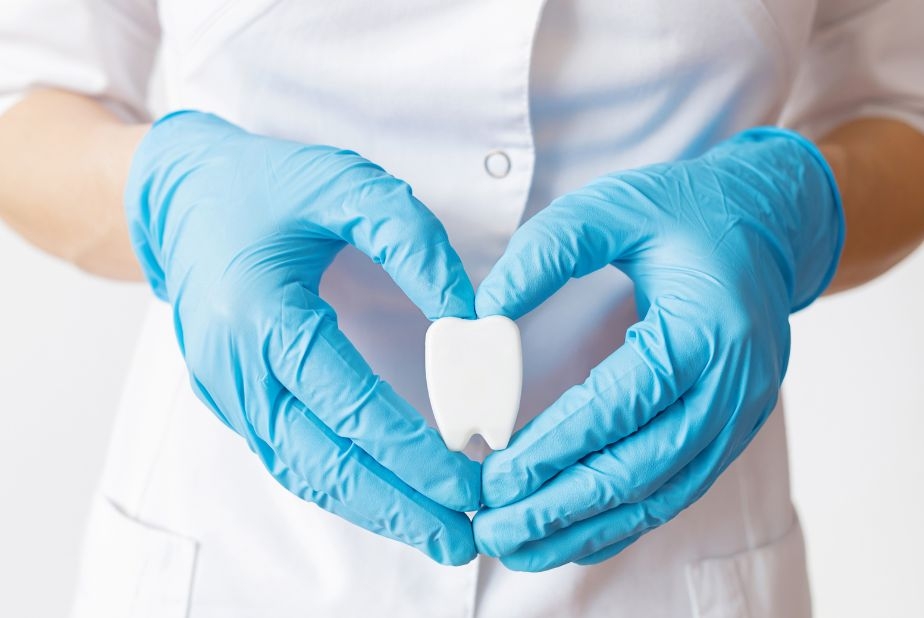 Mani con guanti che formano un cuore con al centro un dente